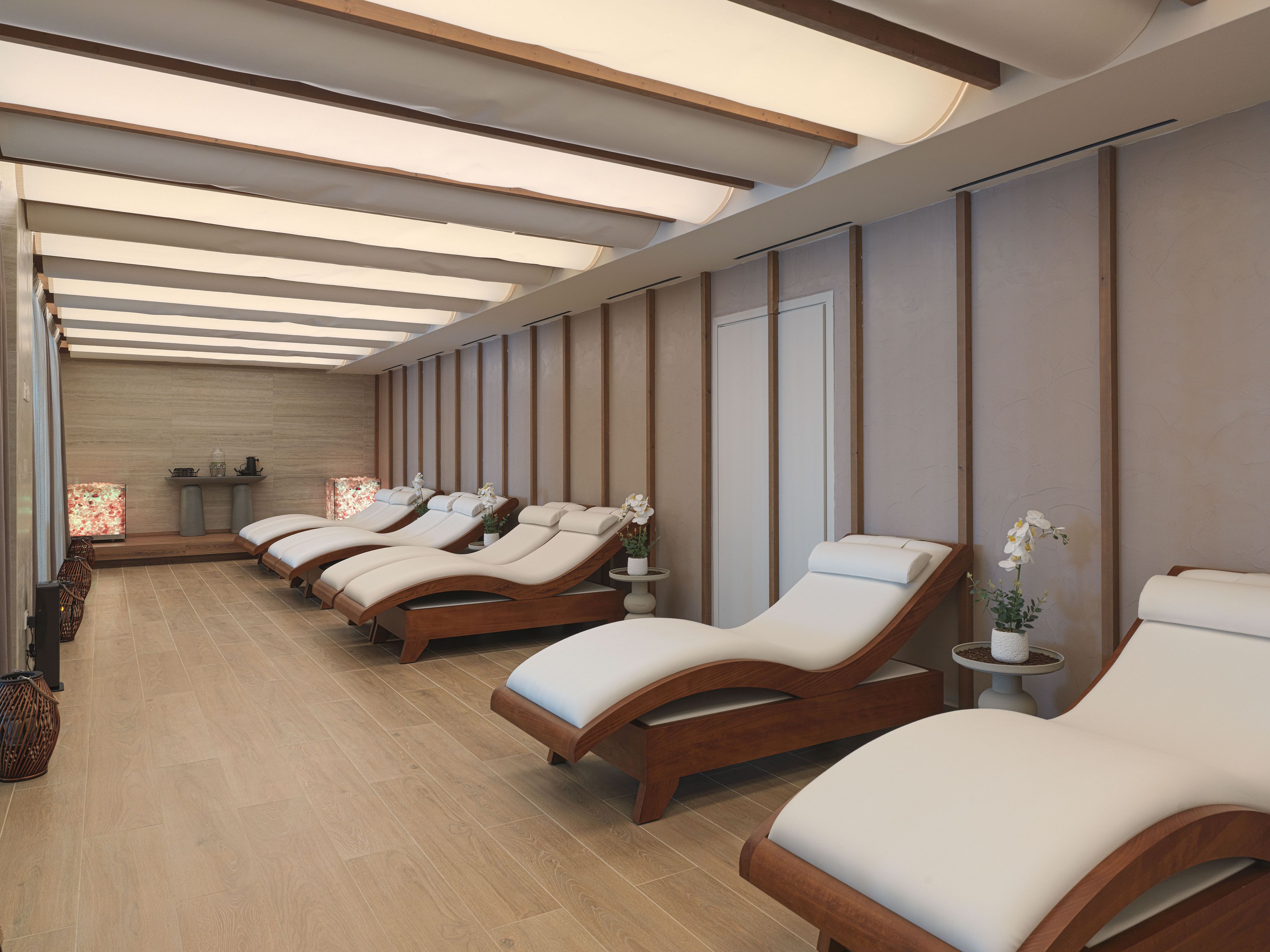 A spa room with multiple sun loungers, a wooden floor, and a ceiling with skylights.