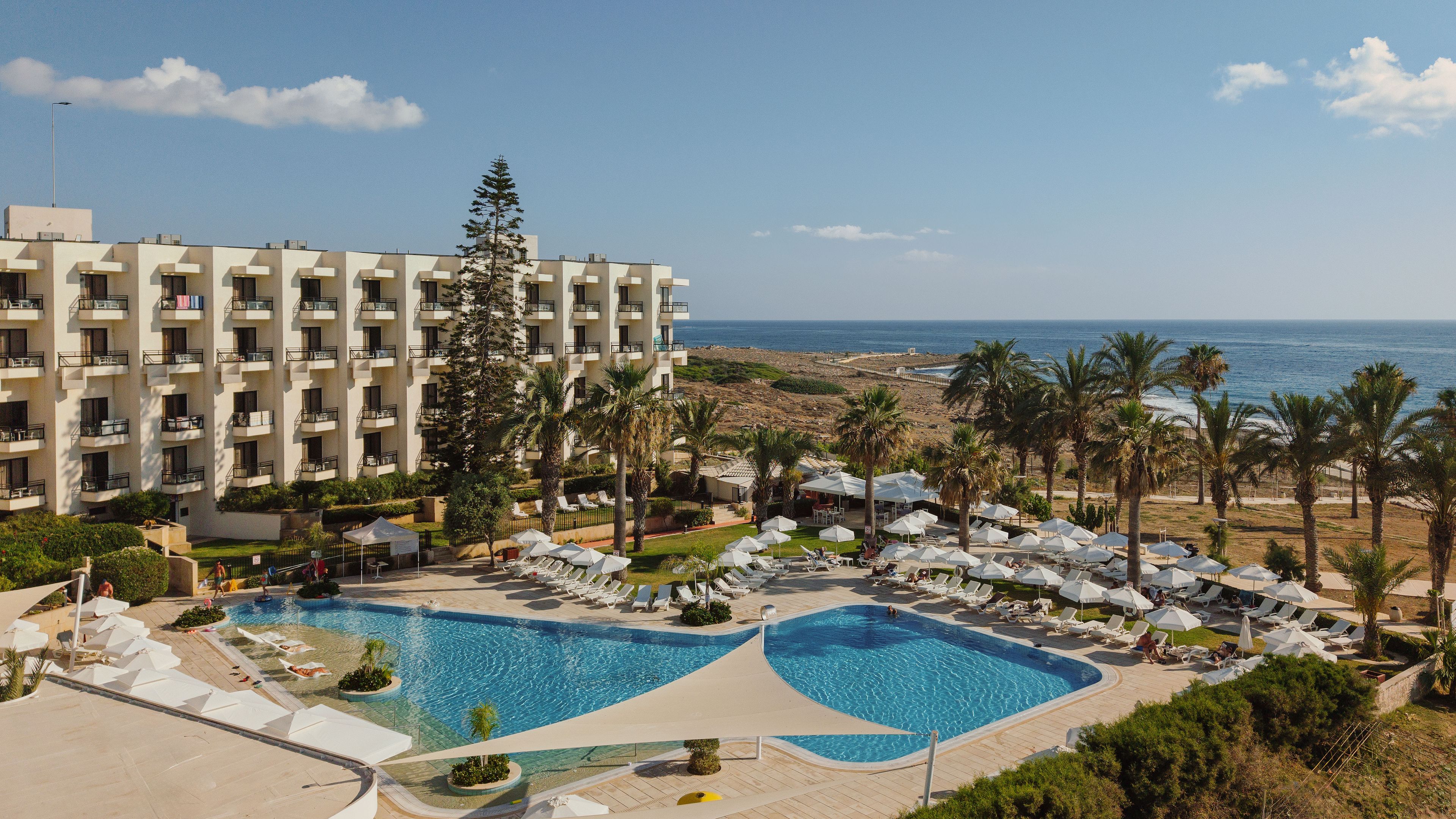 A resort with a swimming pool, lounge chairs, and a view of the ocean.