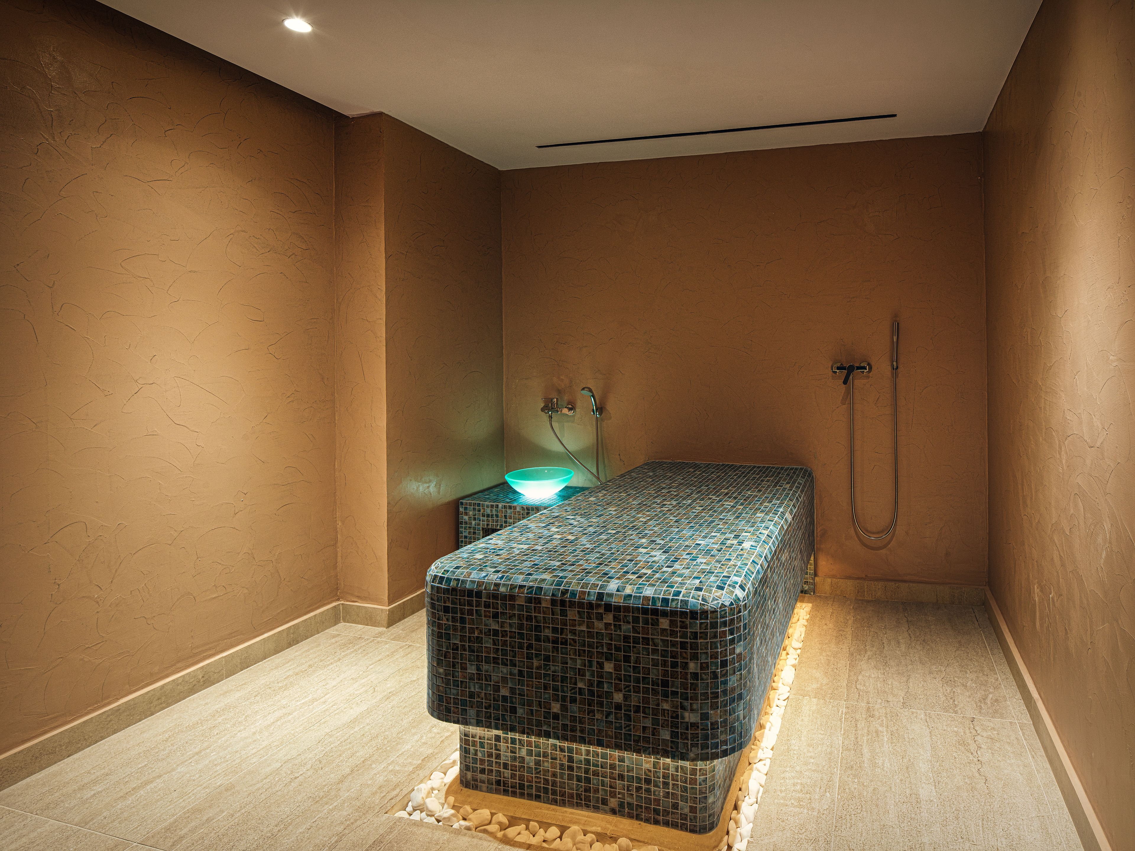 Een spa-ruimte met een betegelde massagetafel, een wastafel en een douche.