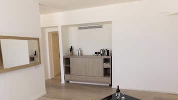 A modern living room with a black coffee table, a small plant, and a fruit basket. There is a kitchen area with wooden cabinets and a sink.