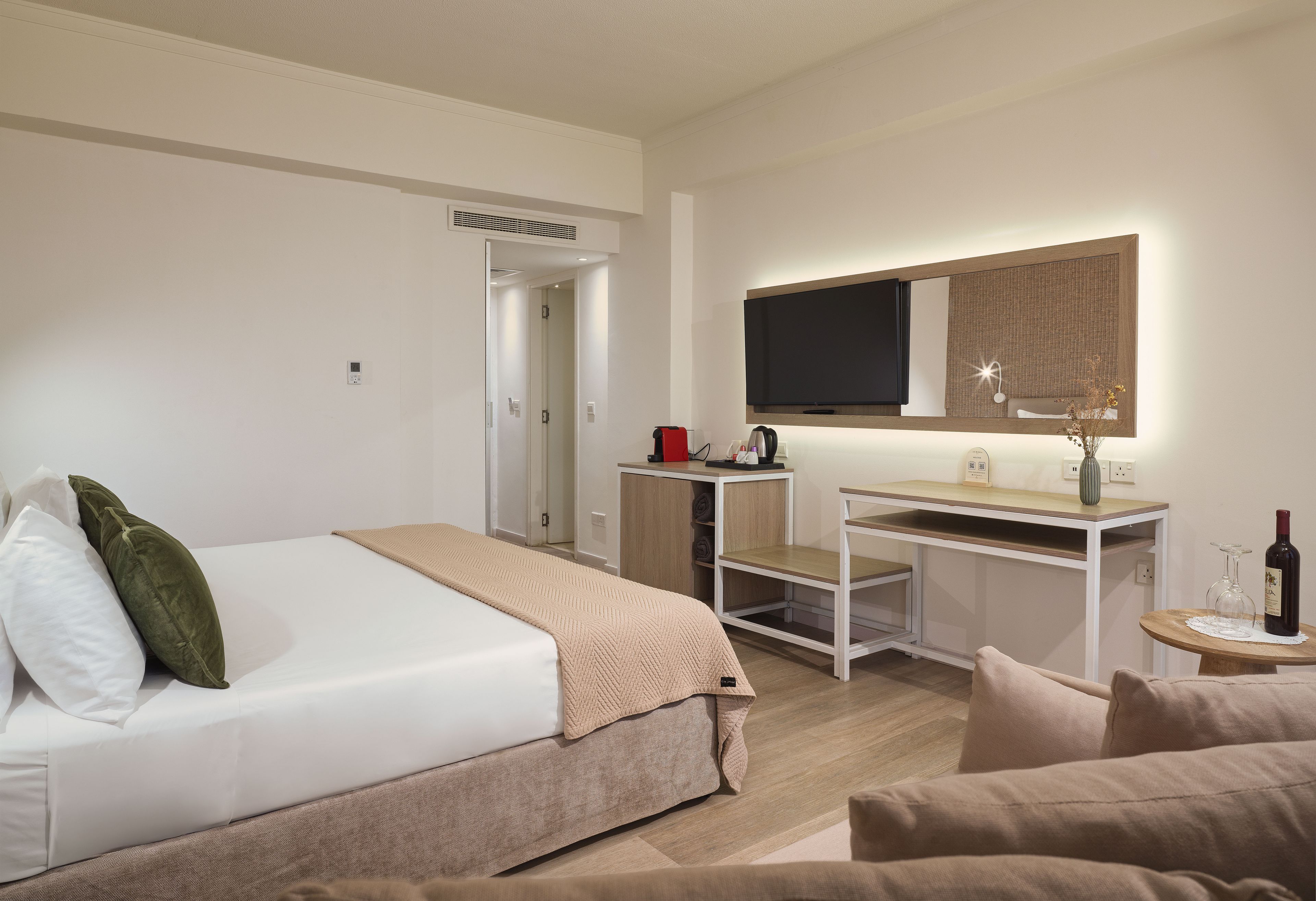 A hotel room with a bed, a desk, a television, and a small table with a bottle and glasses.