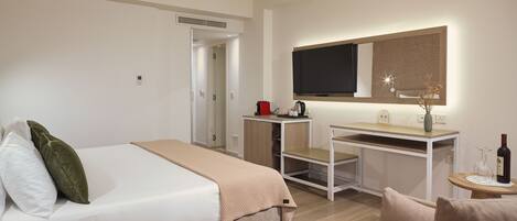 A hotel room with a bed, a desk, a television, and a small table with a bottle and glasses.