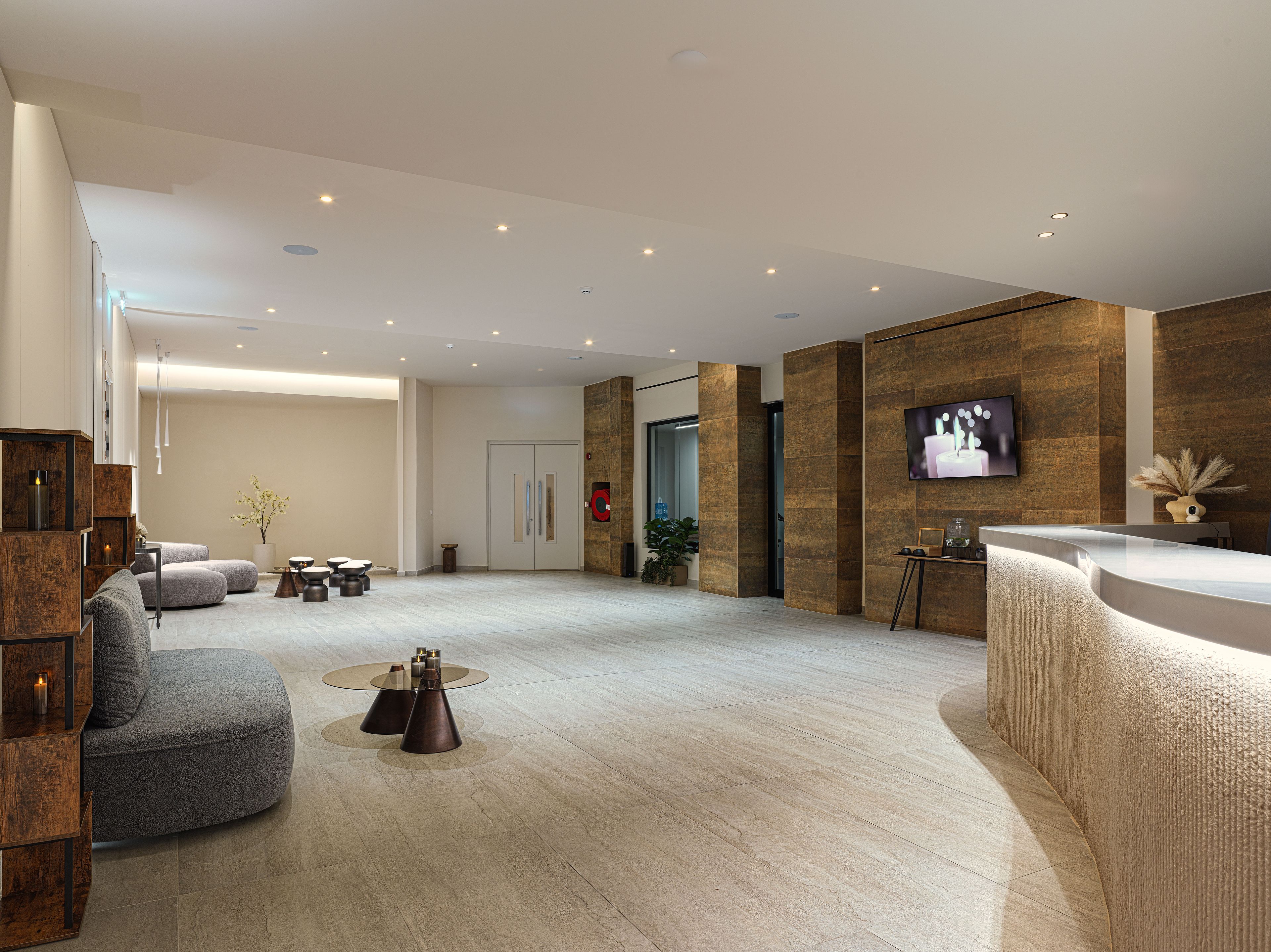Een moderne lobby met een receptiebalie, een zithoek en een grote flatscreen televisie aan de muur.