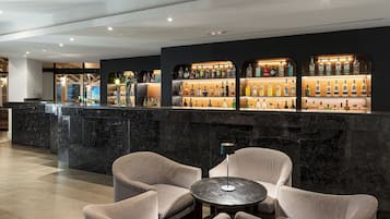 Zona de bar con mostrador de mármol, varias estanterías llenas de botellas de licor y asientos con una mesa redonda.
