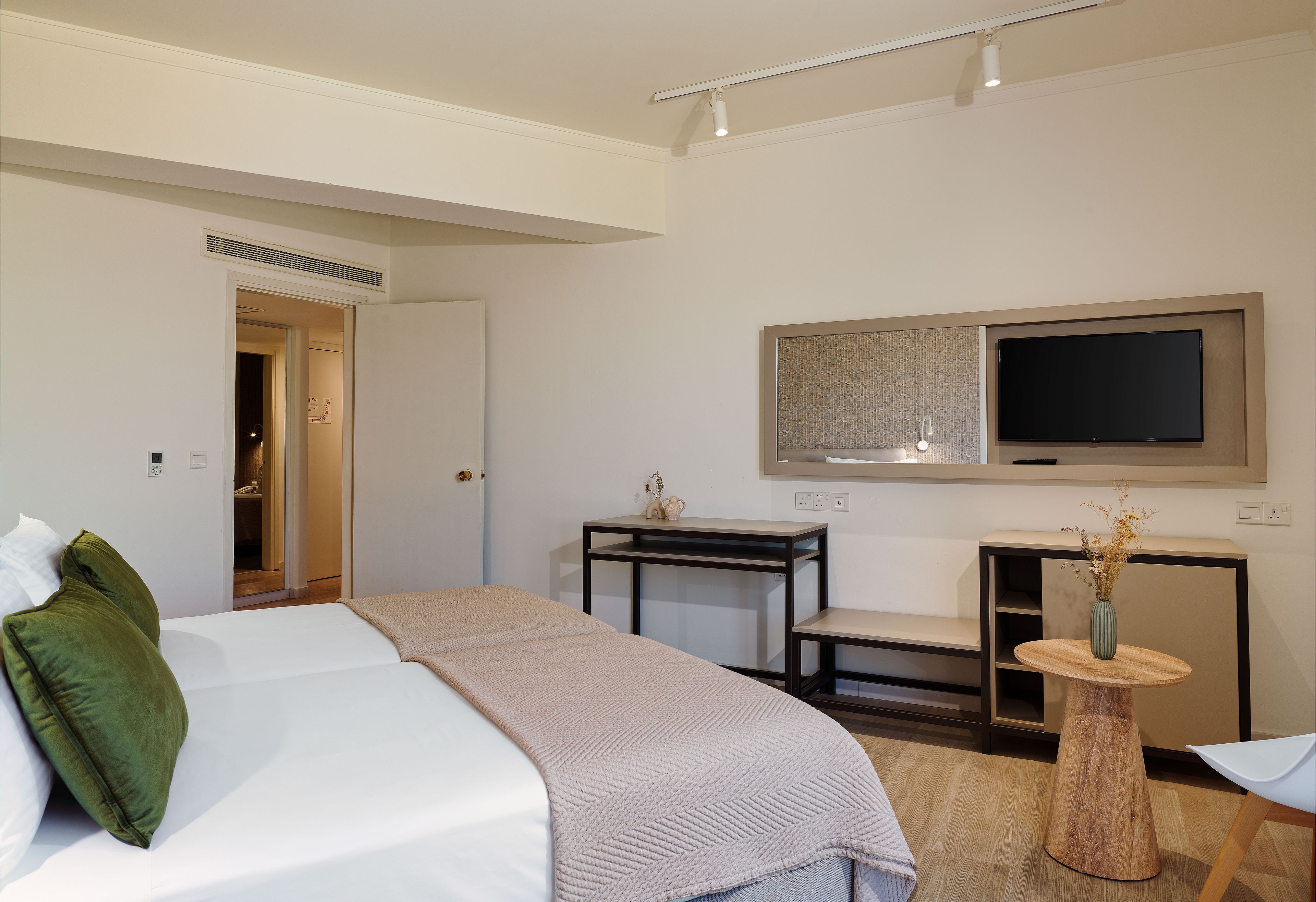 Una habitación de hotel con una cama, un escritorio, un televisor y una mesita con un jarrón.