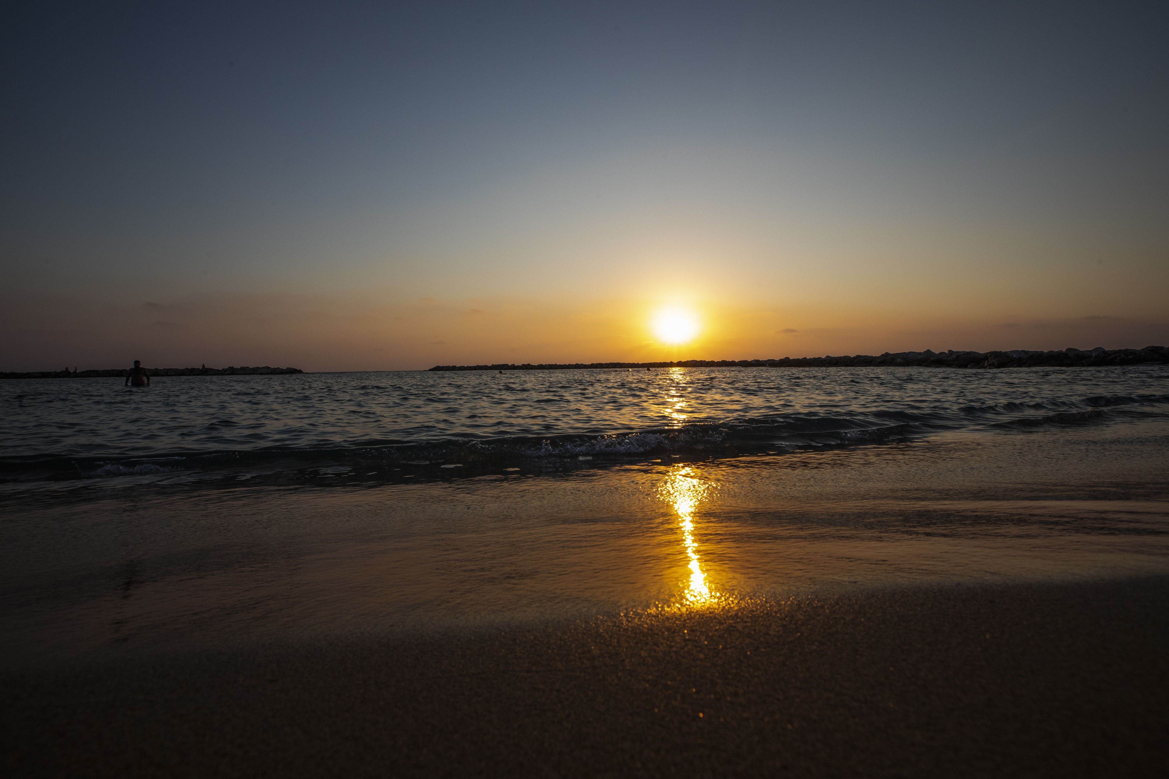 Ein Strand bei Sonnenuntergang, wobei sich die Sonne im Wasser spiegelt.