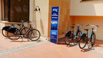 A bike rental station with bicycles parked in front of a building with a signboard advertising bike rentals.