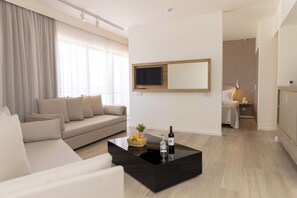A modern living room with a sofa, a coffee table with a wine bottle and glass, and a TV mounted on the wall.