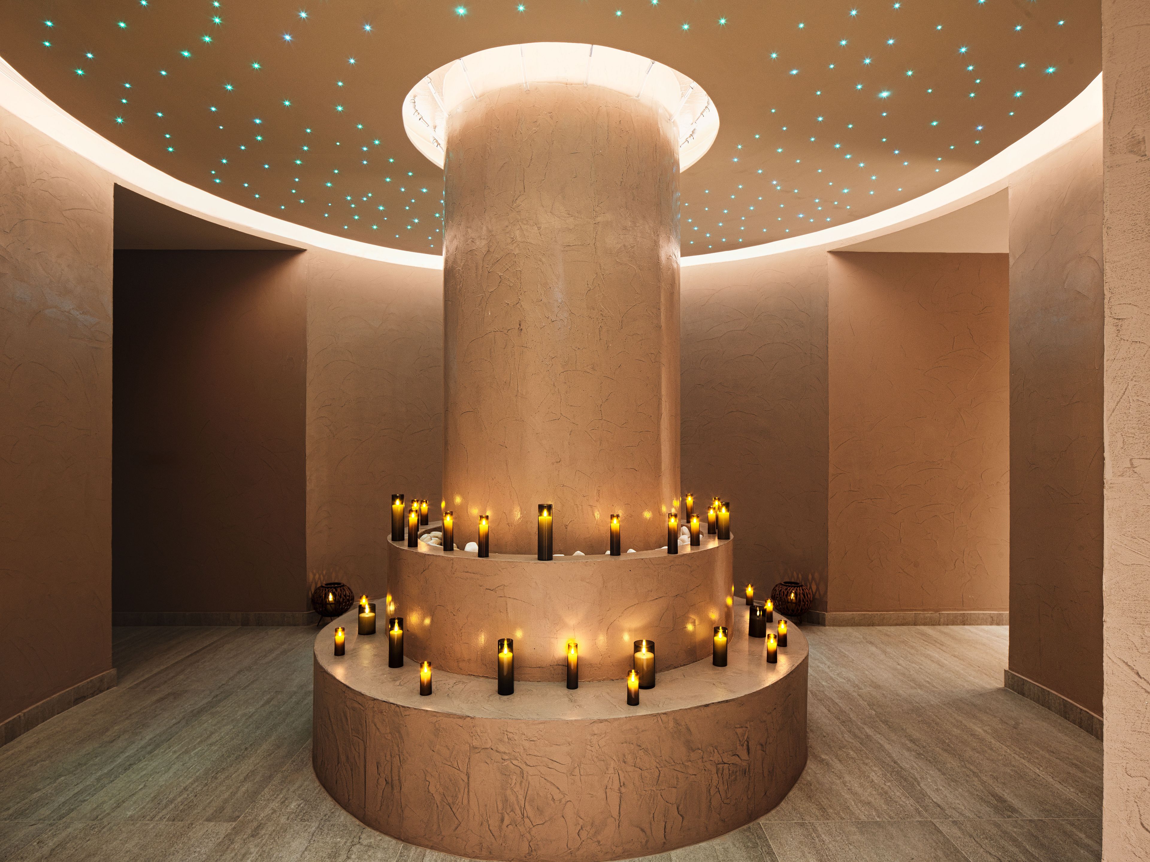 A circular stone structure with candles arranged around it, set against a wall with a textured finish.