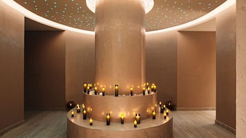 A circular stone structure with candles arranged around it, set against a wall with a textured finish.