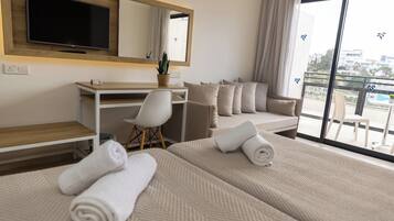 Ein Hotelzimmer mit zwei Betten, einem Schreibtisch, einem Sessel, einem Fernseher und einem Balkon mit Blick.