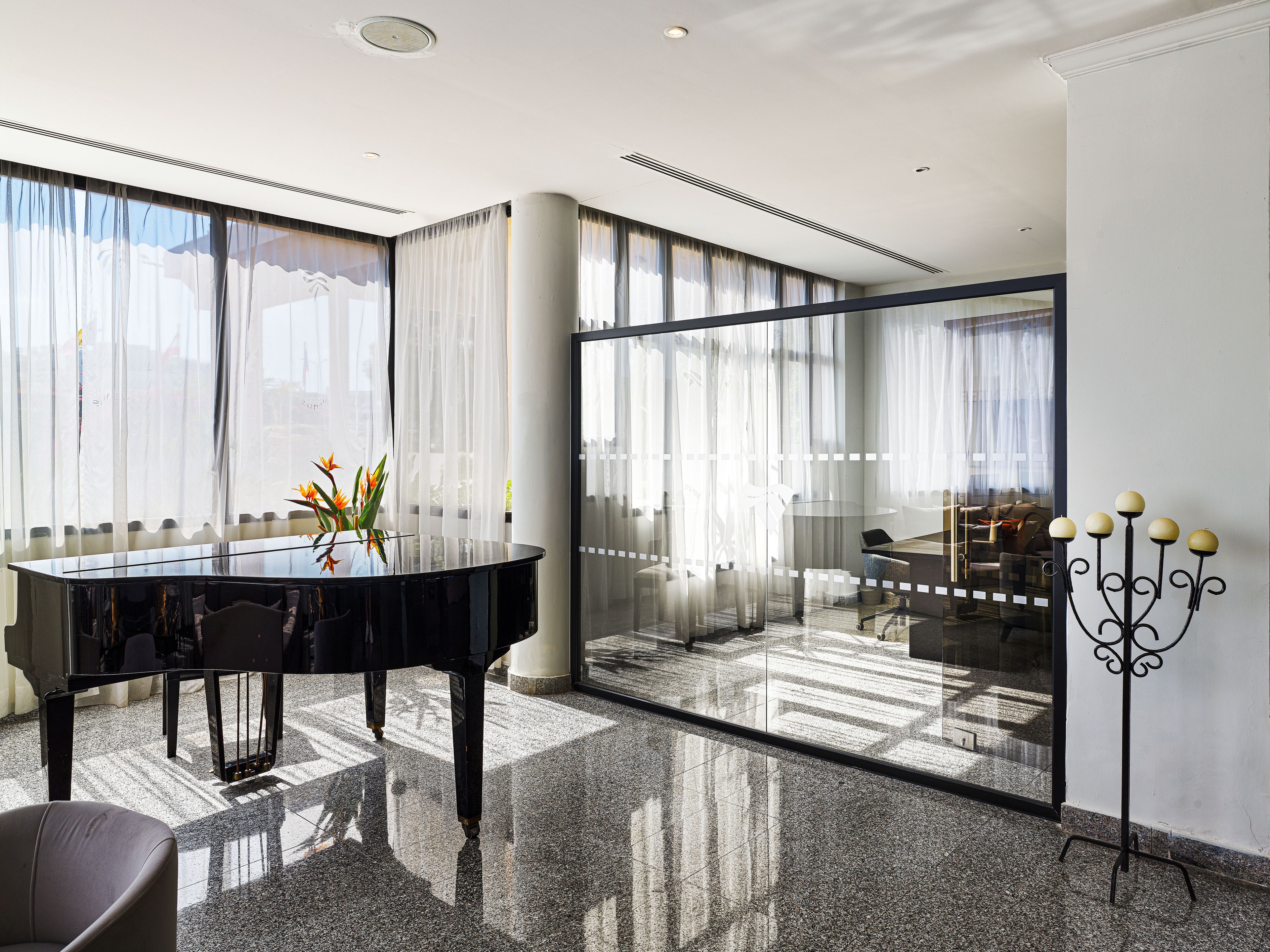 A modern interior with a piano, a glass partition, and a candelabra.