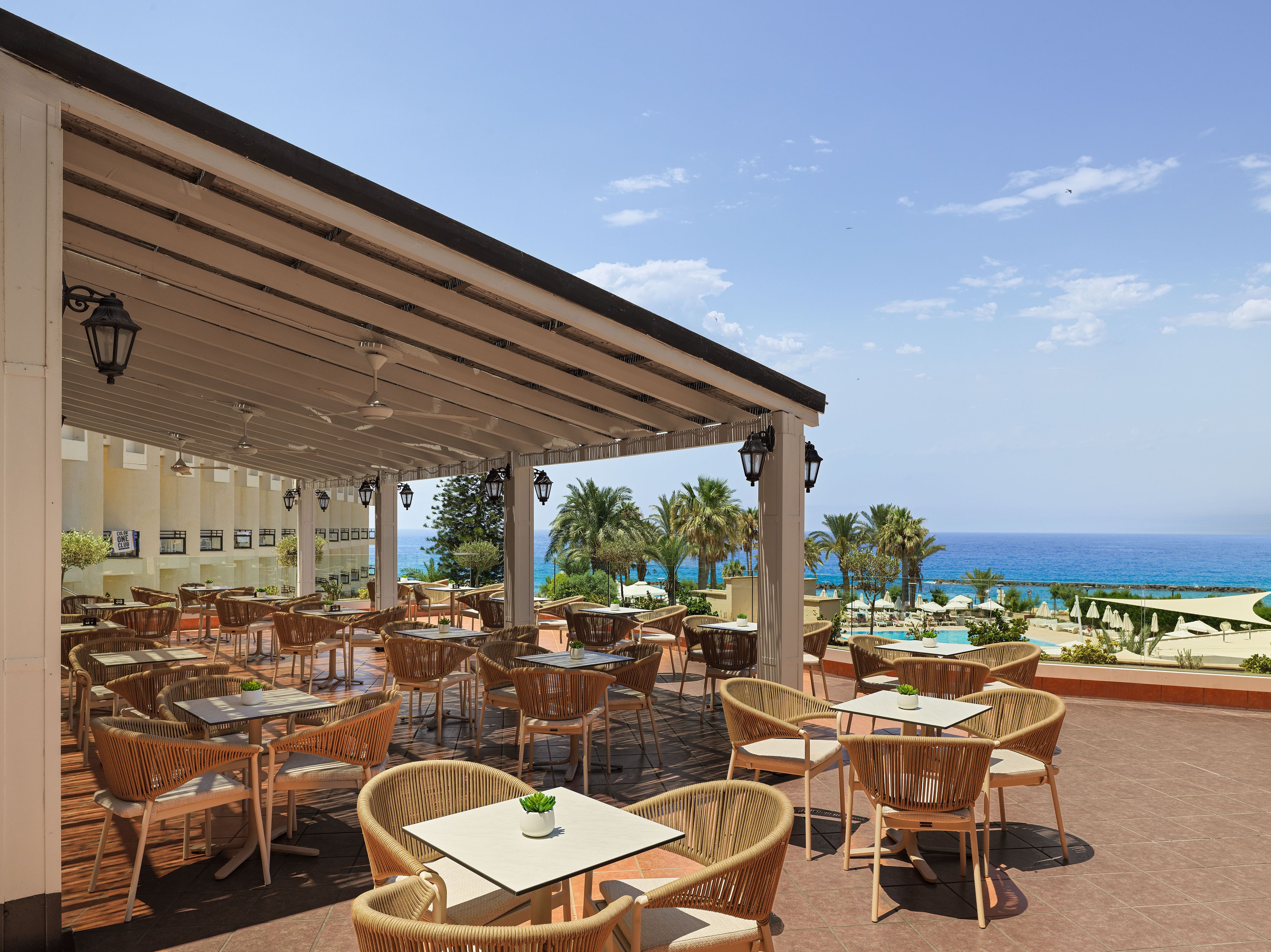 An outdoor cafe with wicker furniture and a view of the sea.