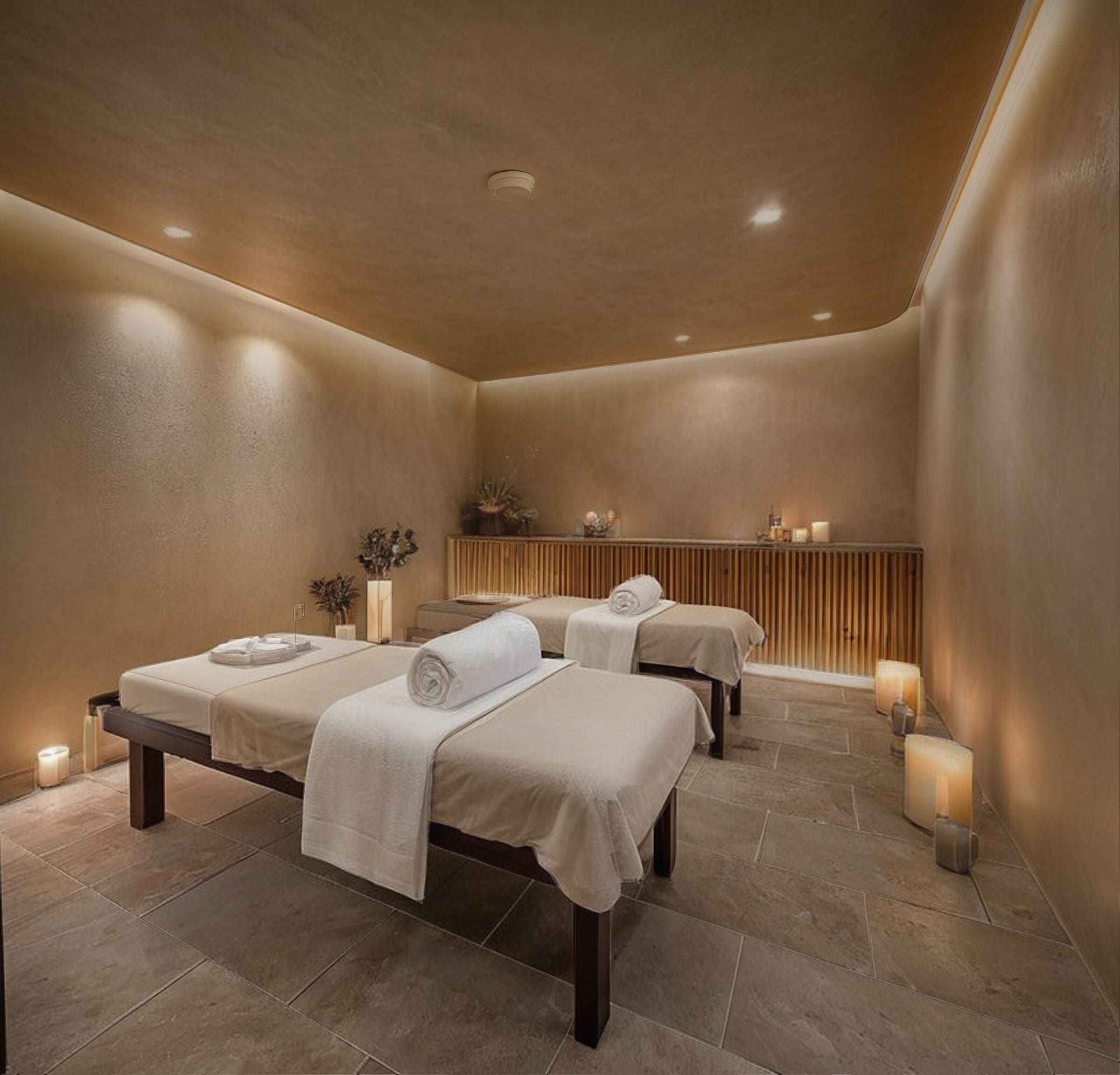 Een wellnessruimte met drie bedden, een houten paneelwand en kaarsen.