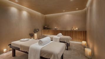 Een wellnessruimte met drie bedden, een houten paneelwand en kaarsen.