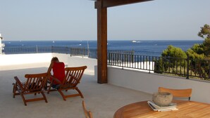 Une terrasse en bois avec vue sur la mer, une table avec un saladier et deux chaises en bois.