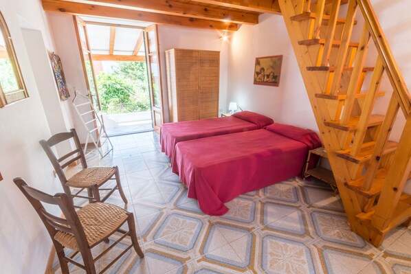 A room with two beds, a wooden staircase, a door leading outside, and a chair.
