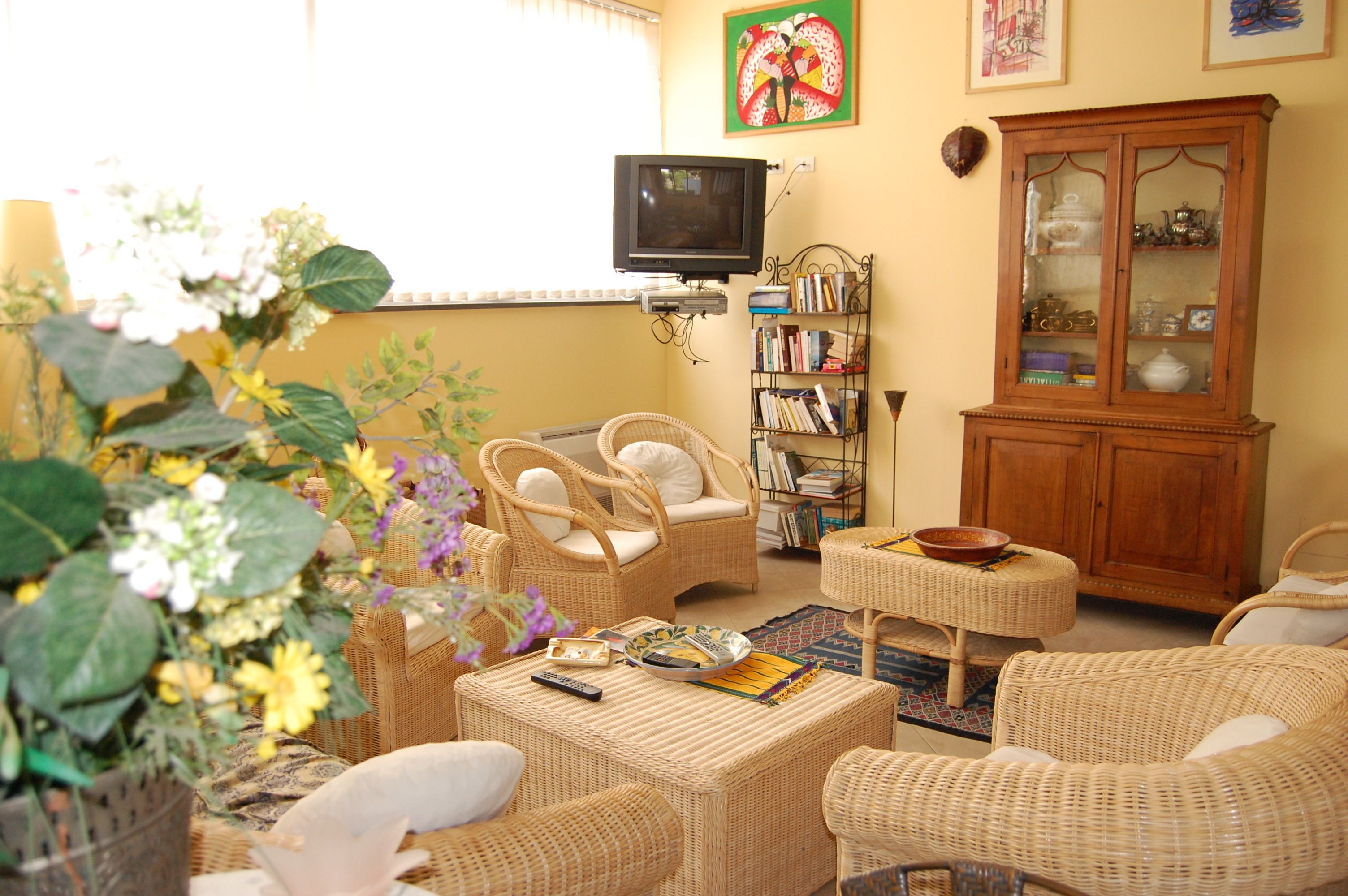 Una sala de estar acogedora con muebles de mimbre, un televisor, una estantería y un aparador.