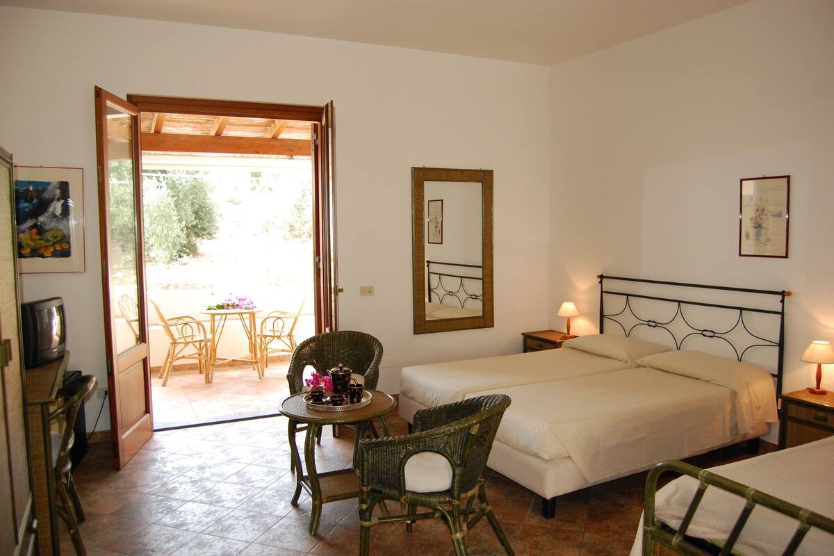 A bedroom with two beds, a dining table with chairs, a TV, and a balcony.