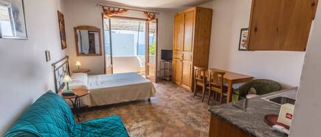 Una habitación pequeña con cama, un escritorio, una silla y una kitchenette.