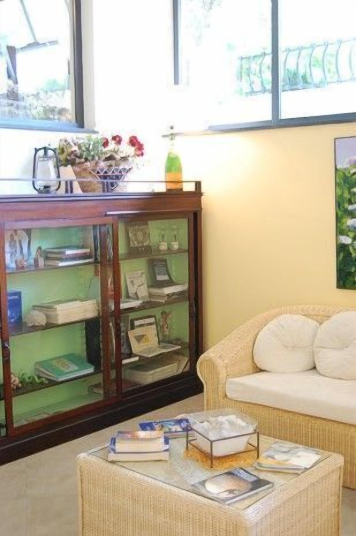 Una sala de estar con un sofá, un aparador de vidrio con libros y una mesa de centro con libros y revistas.