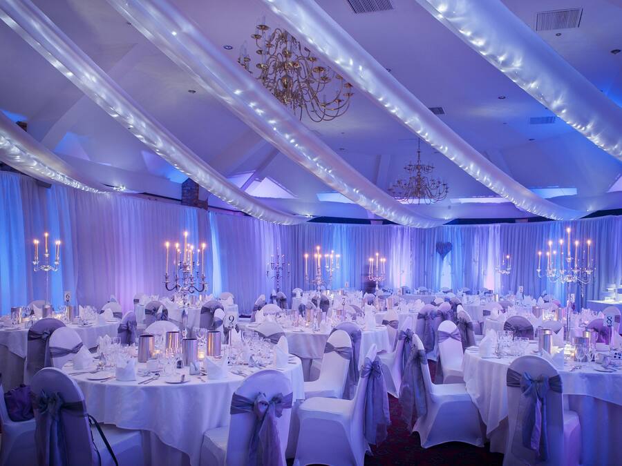 A banquet hall with round tables set for a formal event, featuring white tablecloths and chairs with blue sashes.