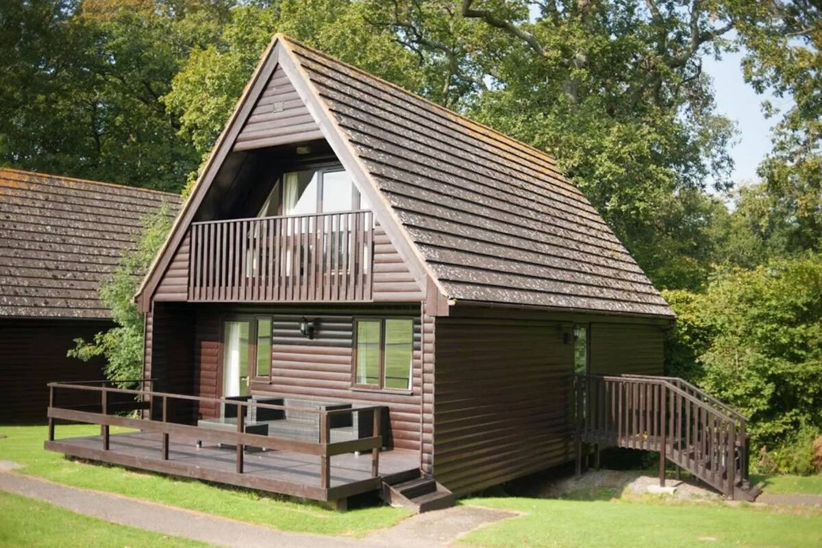 A wooden cabin with a balcony, a porch, and a staircase leading to the entrance.
