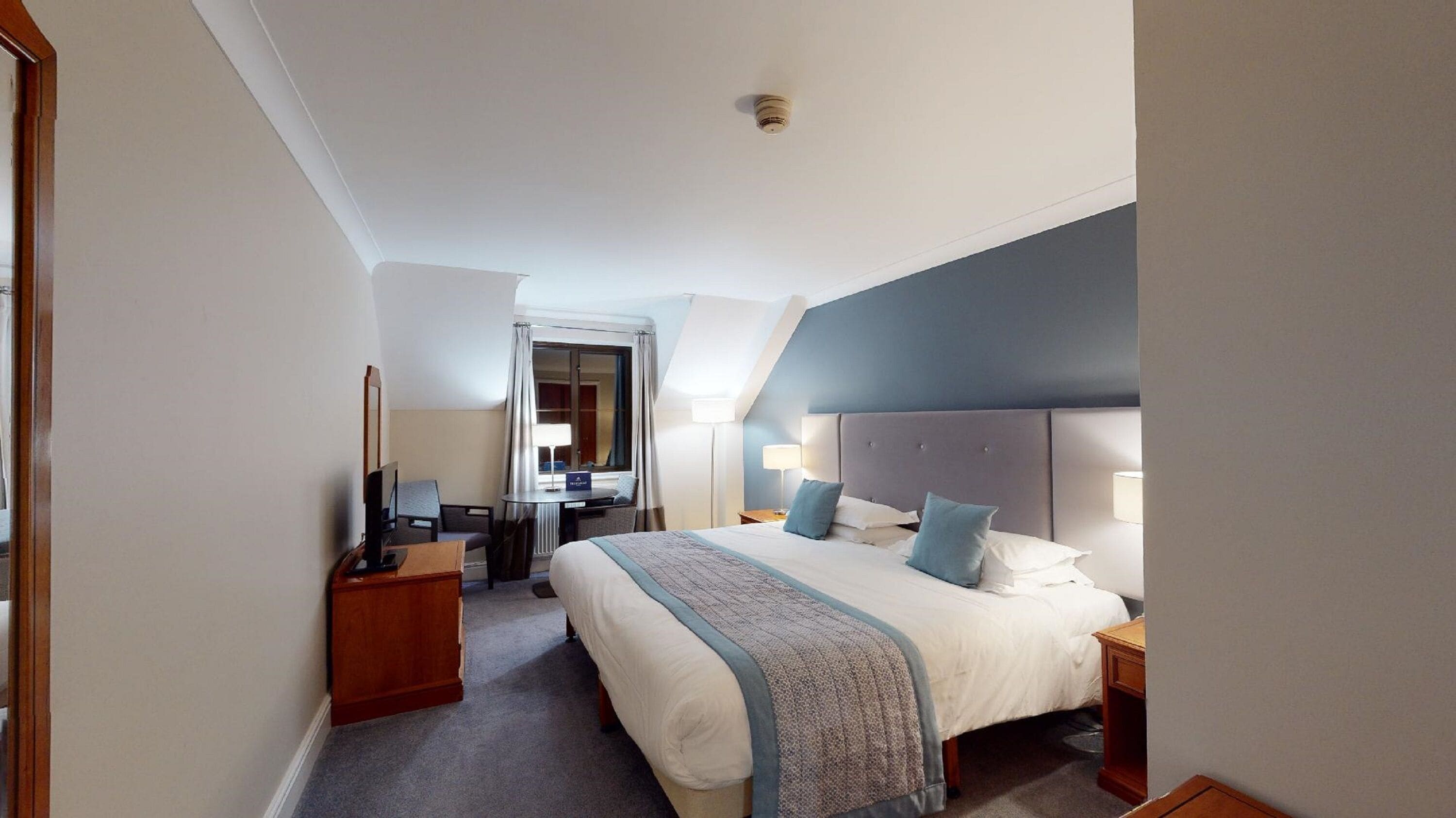 Une chambre d’hôtel avec un grand lit, des tables de chevet, un bureau et un miroir.