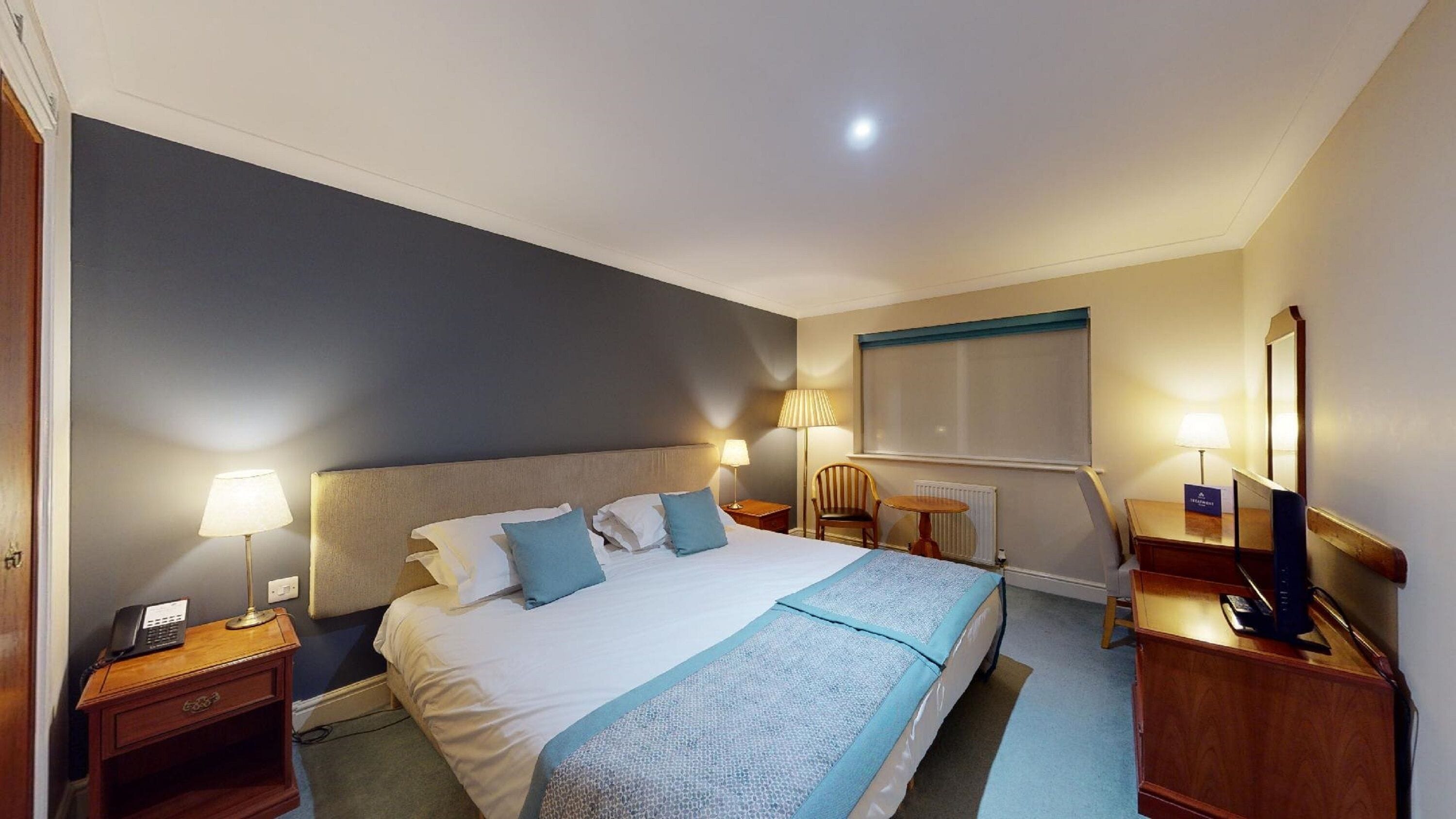A hotel room with a large bed, bedside lamps, a desk with a computer, and a chair.