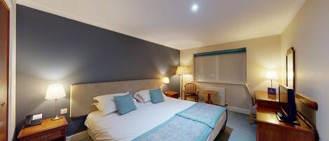 A hotel room with a large bed, bedside lamps, a desk with a computer, and a chair.
