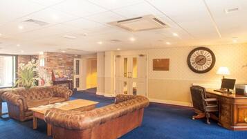A lobby with leather sofas, a wooden desk, and a clock on the wall.
