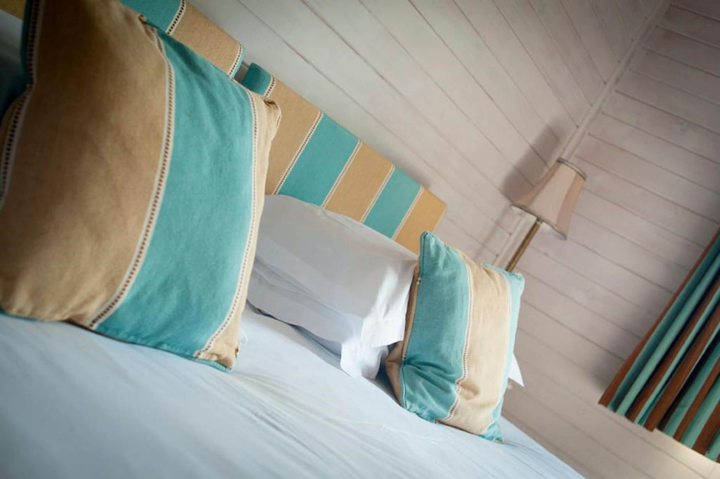 A bed with teal and beige pillows, a striped headboard, and a wooden ceiling.