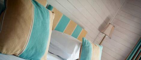 A bed with teal and beige pillows, a striped headboard, and a wooden ceiling.