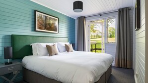 Un dormitorio con una cama grande, una mesita de noche, una lámpara, un cuadro en la pared y vistas al exterior a través de una puerta.