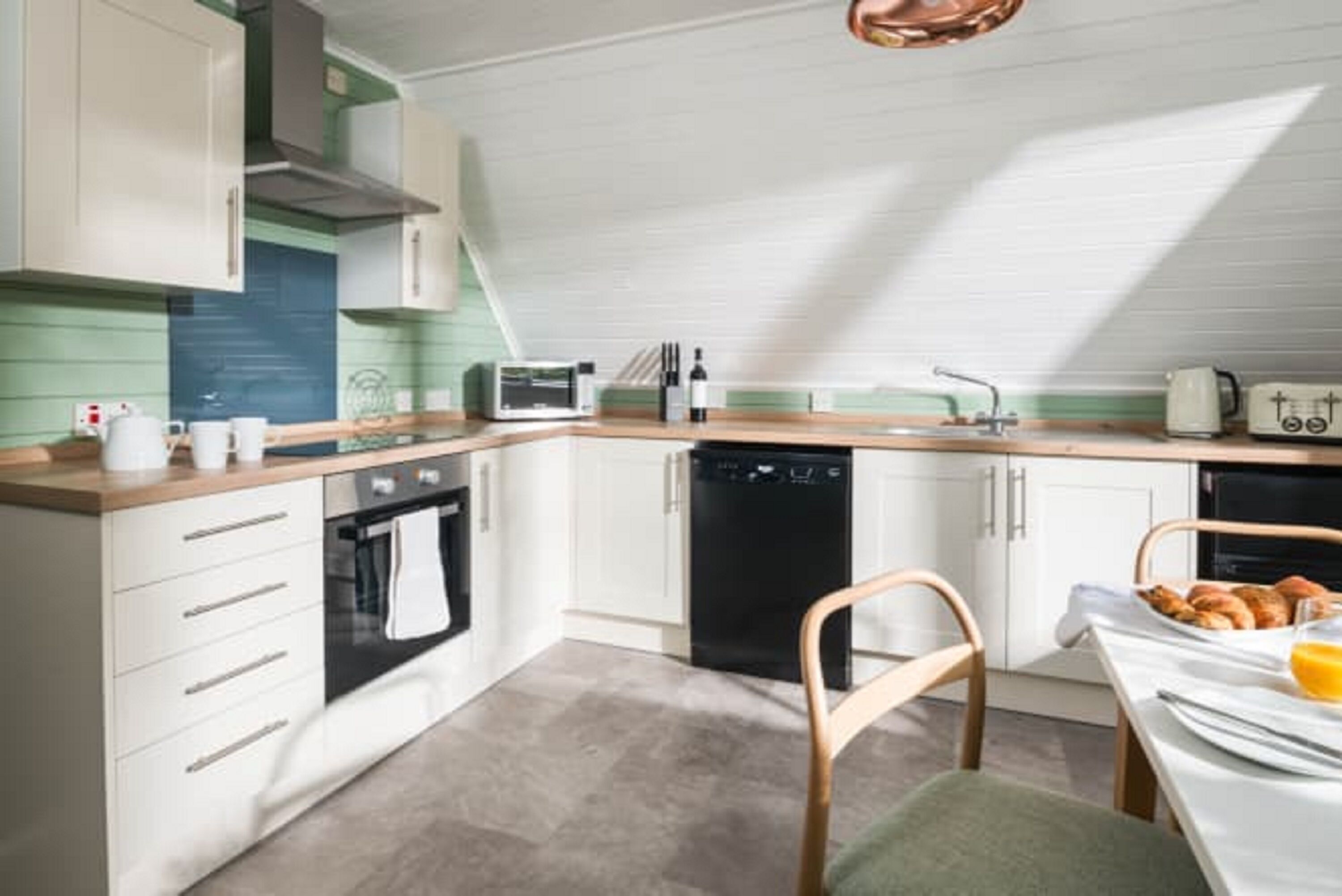 Une cuisine moderne avec des meubles blancs, un four à micro-ondes, un lave-vaisselle et un coin repas avec une table mise pour le petit-déjeuner.