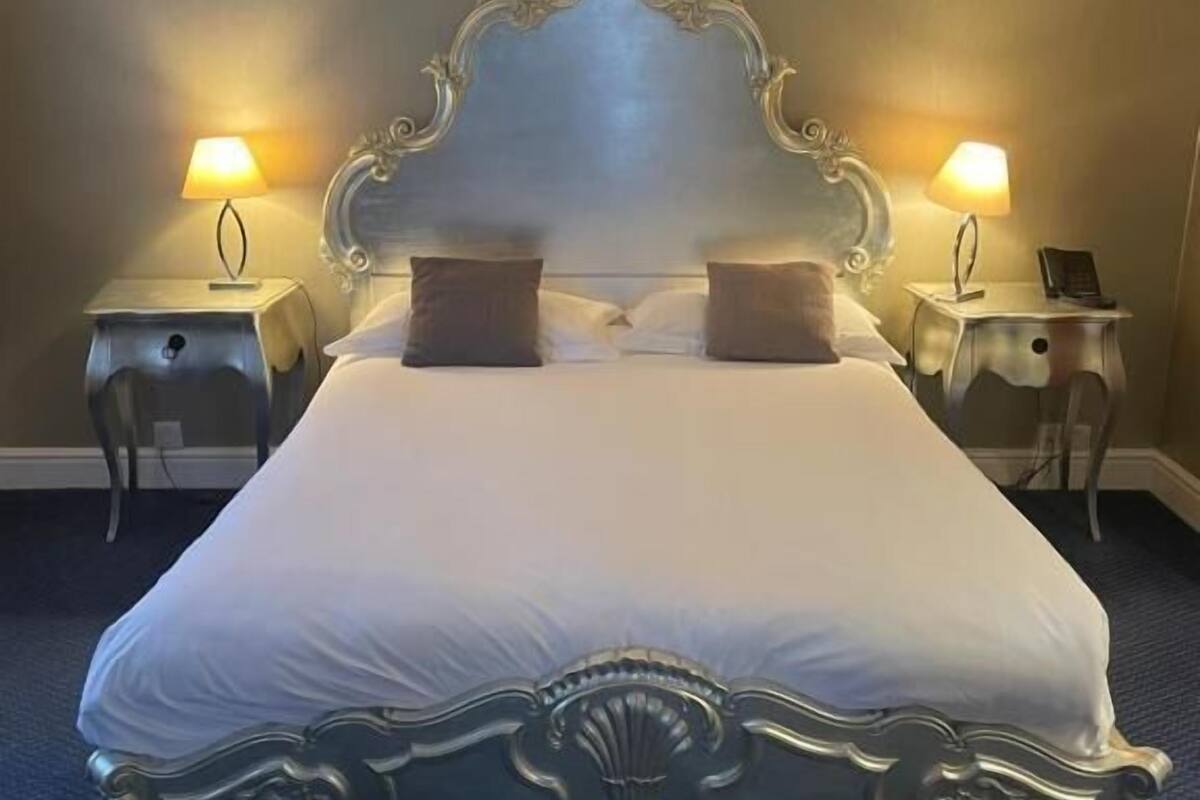 A double bed with an ornate headboard, two bedside tables with lamps, and a dark carpeted floor.