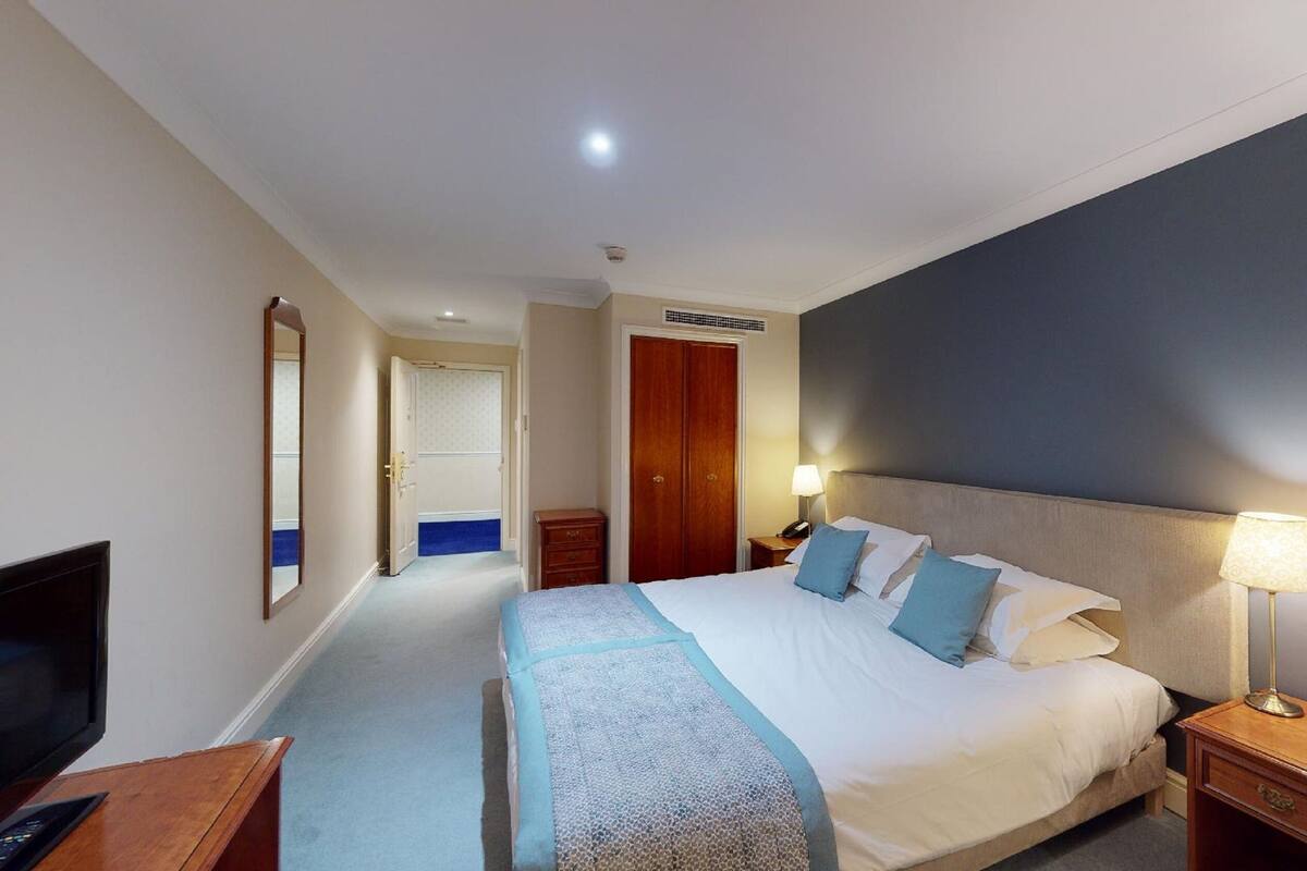 A hotel room with a large bed, bedside lamps, a TV, and a wardrobe.