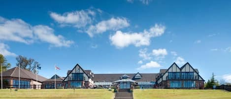 A large building with a central entrance and multiple wings, surrounded by a well-maintained lawn.