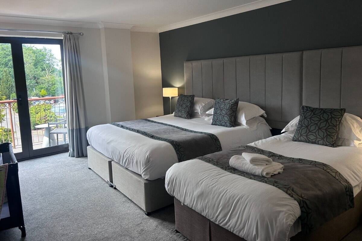 A hotel room with two beds, a balcony, and a view of greenery.