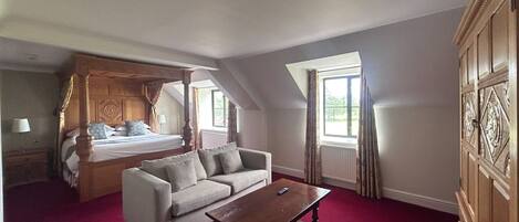 A bedroom with a four-poster bed, a sofa, a wooden coffee table, and a large window with curtains.
