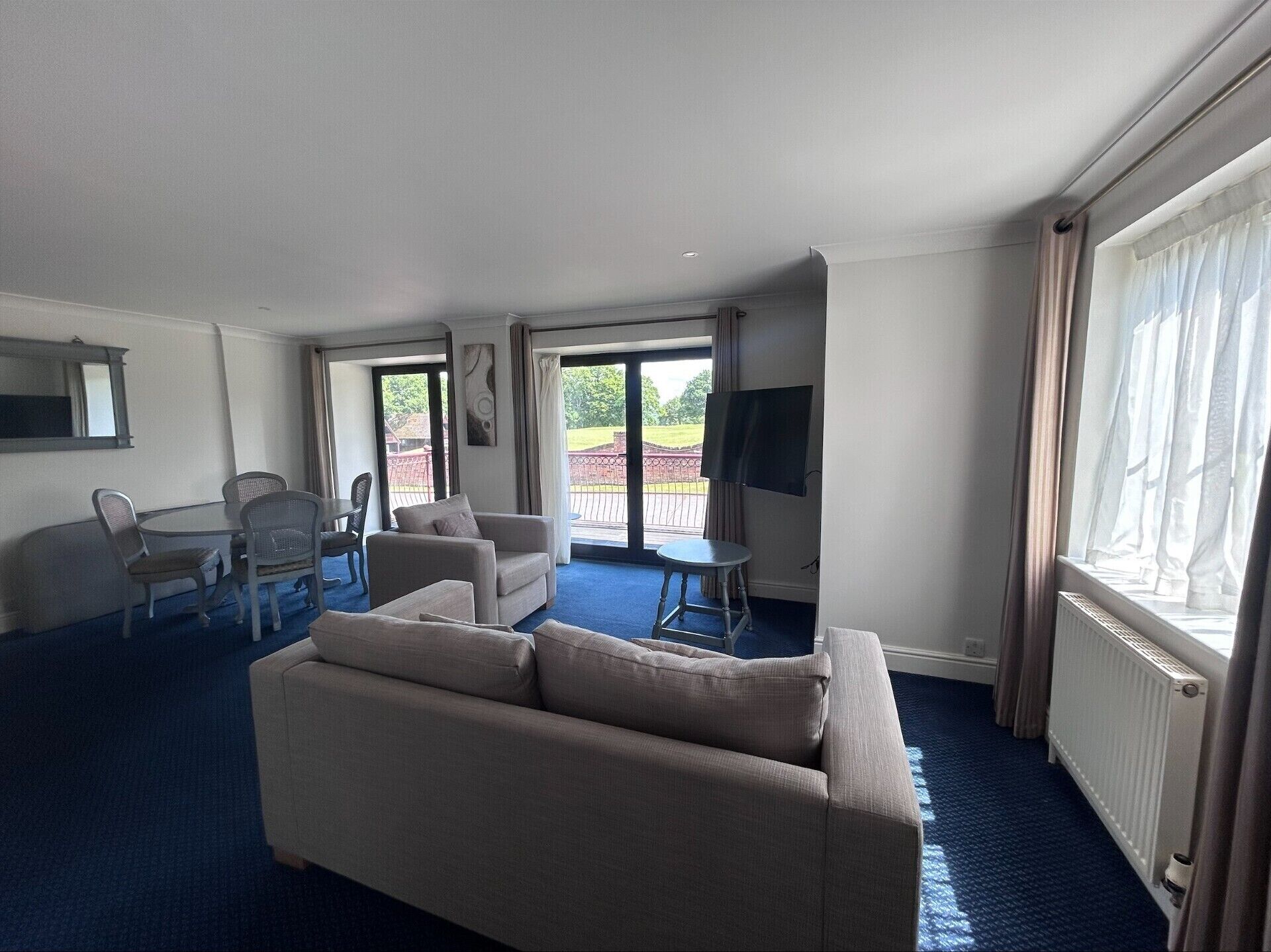 A hotel room with a sofa, a dining table with chairs, a TV, and a view of the outdoors.