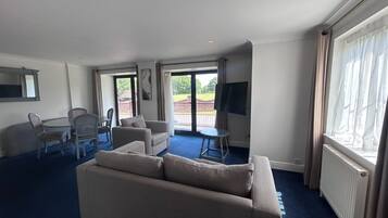 A hotel room with a sofa, a dining table with chairs, a TV, and a view of the outdoors.