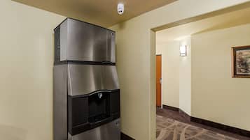 A hallway with a stainless steel refrigerator and a water dispenser, a framed picture on the wall, and a carpeted floor.