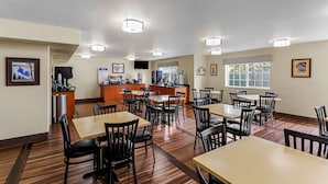 A dining area with multiple tables and chairs, a kitchen area with a counter and appliances, and framed pictures on the walls. - Best Western Rose Quartz Inn (Chester)