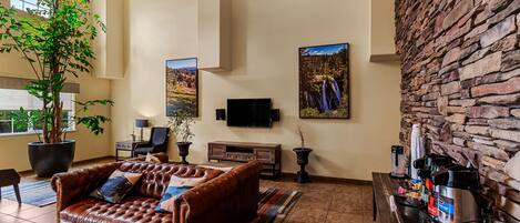 A spacious living area with a leather sofa, a large potted plant, a stone wall, and a coffee station.