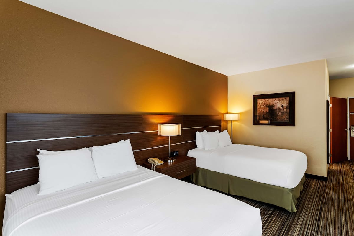 A hotel room with two beds, a wooden headboard, bedside lamps, a framed picture on the wall, and a carpeted floor.