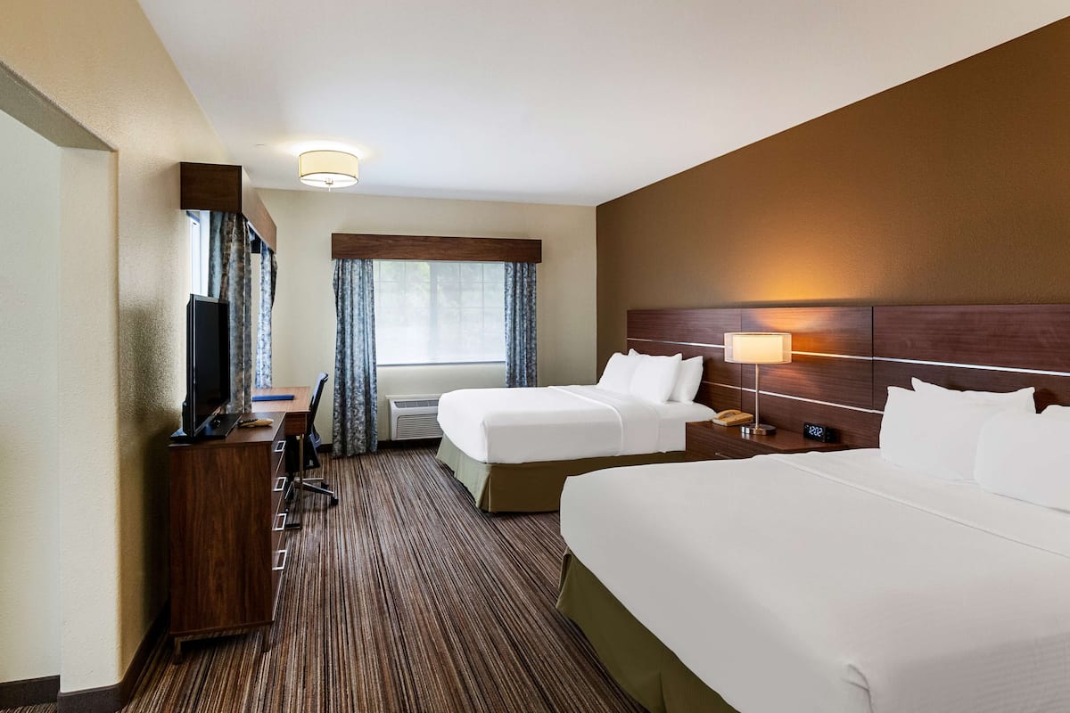 A hotel room with two beds, a desk, a television, and a window with curtains.