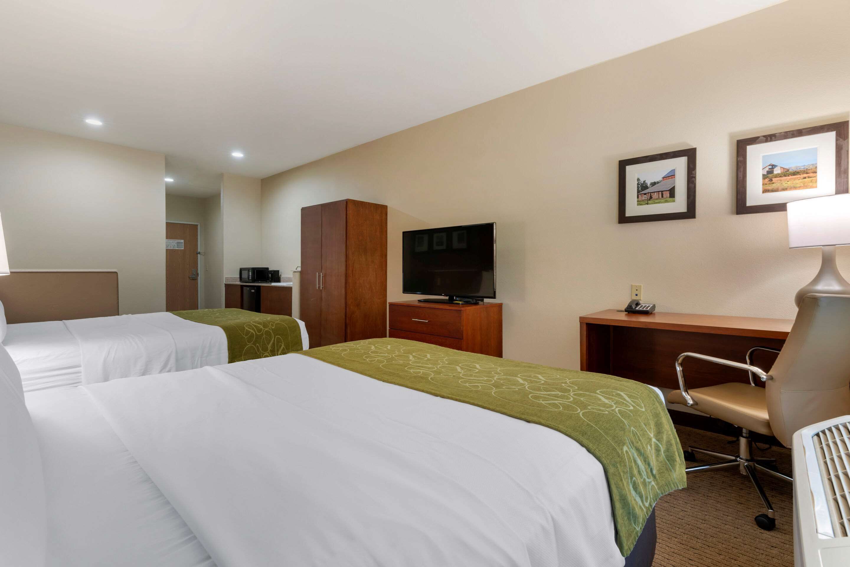 A hotel room with two beds, a desk, a television, and a chair.