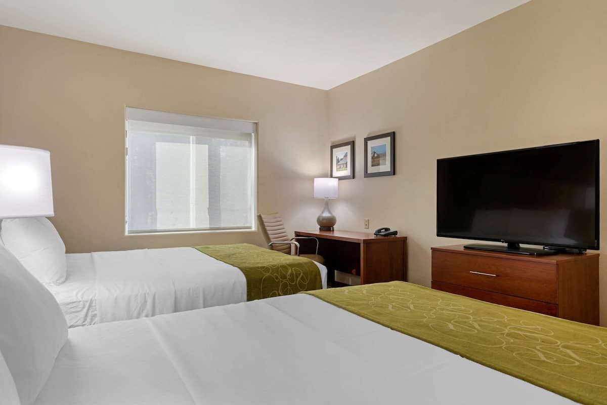 A hotel room with two beds, a desk, a television, and a window.