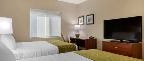 A hotel room with two beds, a desk, a television, and a window.